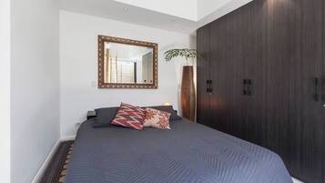 A bedroom with a large bed, a mirror, a wardrobe, and a plant.