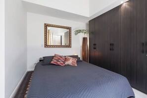 Ein Schlafzimmer mit einem großen Bett, einem Spiegel, einem Kleiderschrank und einer Pflanze.