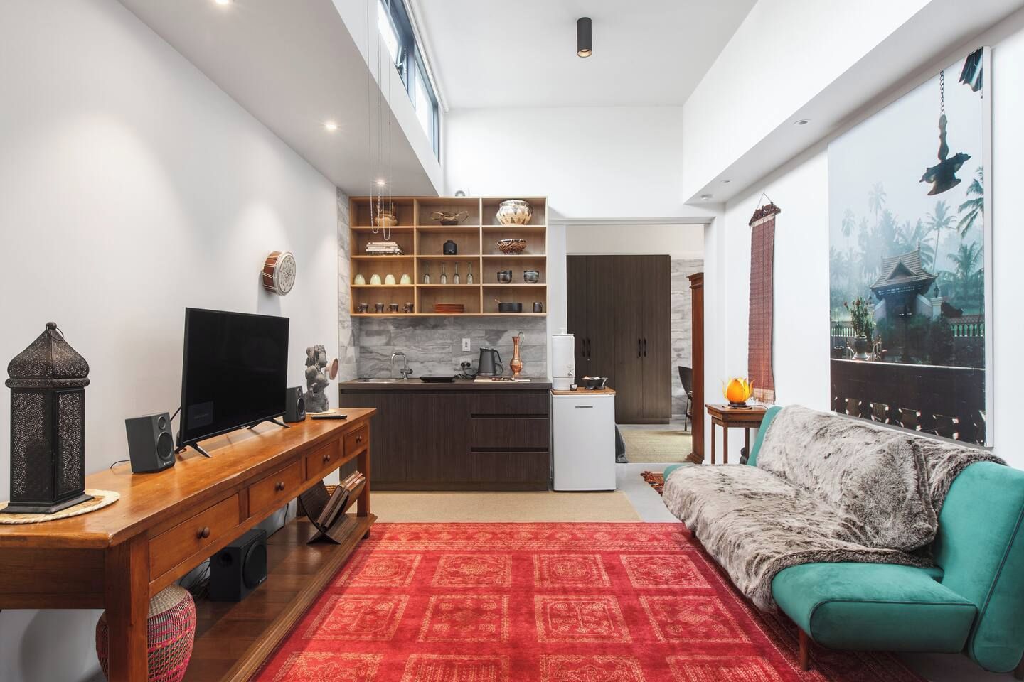 A modern living room with a television, a wooden desk, and a red patterned rug.