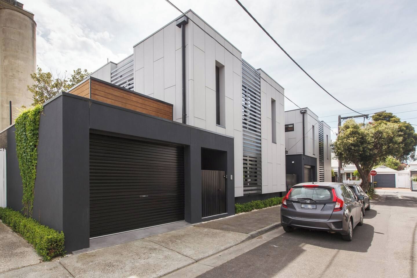 A modern residential building with a garage, a car parked in front, and a tree nearby.