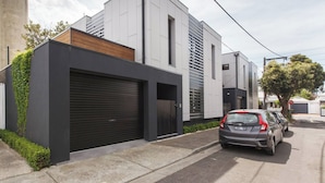 Un edifici residencial modern amb un garatge, un cotxe a la façana i un arbre a prop.