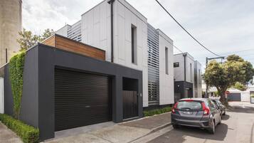A modern residential building with a garage, a car parked in front, and a tree nearby.