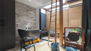 A modern bathroom with a freestanding bathtub, a wooden ladder, and a view of an outdoor seating area.