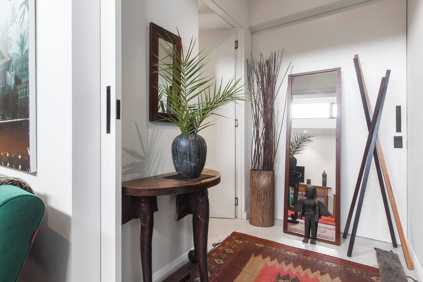 A hallway with a round wooden table, a potted plant, a mirror, and a statue.