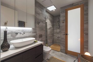 Ein modernes Badezimmer mit einem großzügigen freistehenden Waschtisch, einer Toilette und einer begehbaren Dusche.