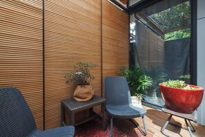 Un espacio exterior moderno con asientos, una pared de listones de madera, una mesita con una planta y dos sillas.