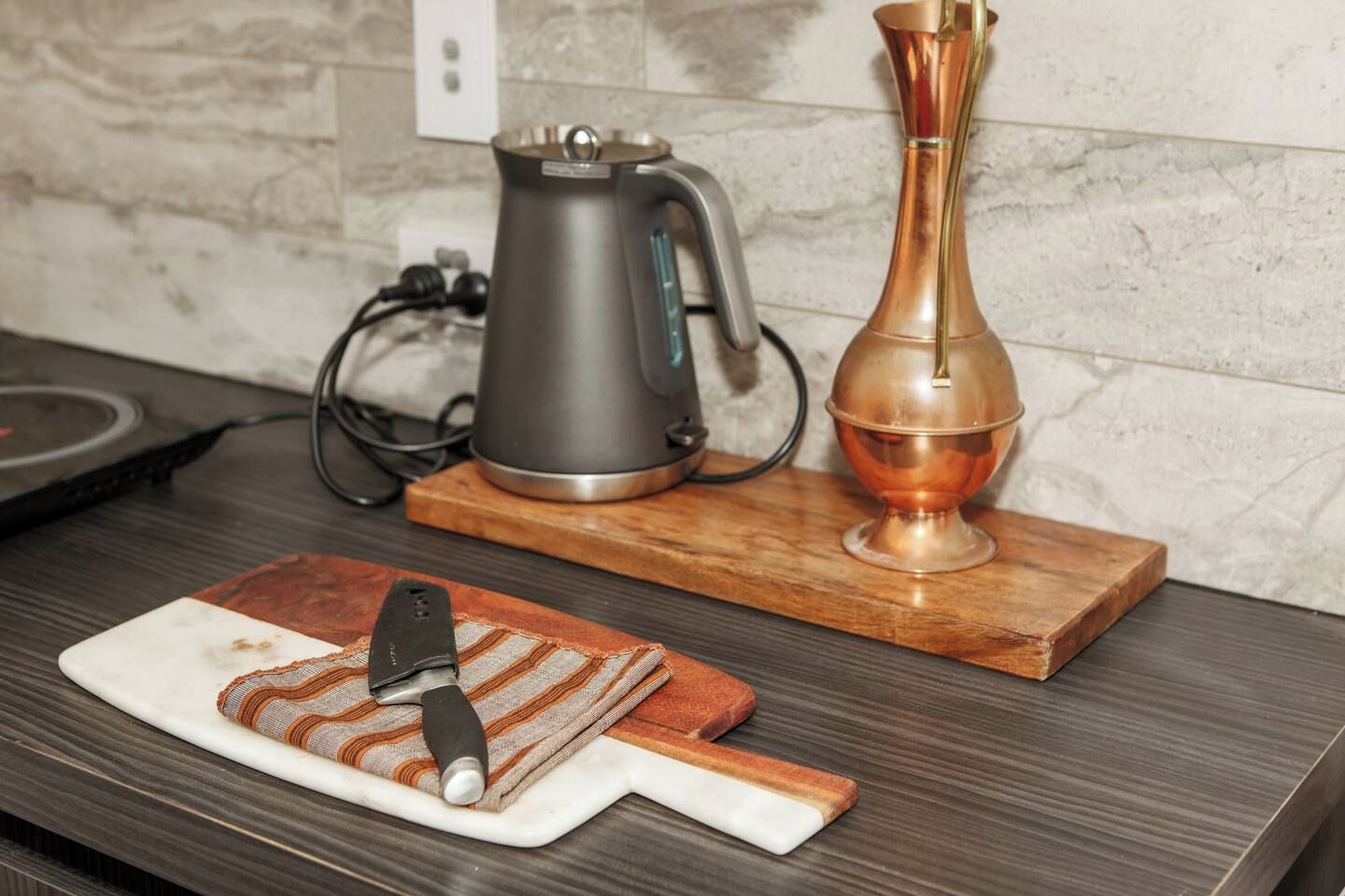 A kitchen counter with a coffee maker, a copper vase, and a cutting board with a knife.