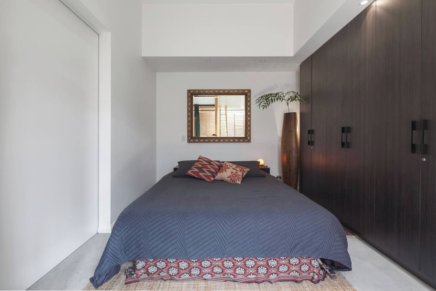 A bedroom with a large bed, a mirror, a wardrobe, and a plant.