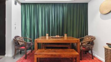 A dining area with a wooden table and benches, a green curtain backdrop, and a red patterned rug.
