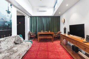 Una sala de estar con un sofá, una mesa de comedor con sillas, un televisor y altavoces.