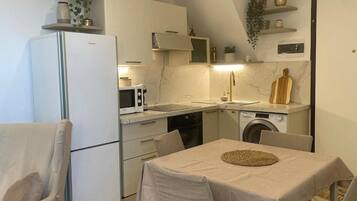 Cocina compacta con refrigerador, microondas, pileta y lavadora. Hay una mesa de comedor con sillas y una planta colgante.