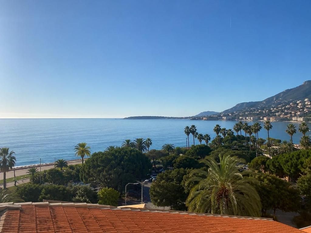 Un paisaje costero con vista despejada al mar, palmeras y una ciudad distante.