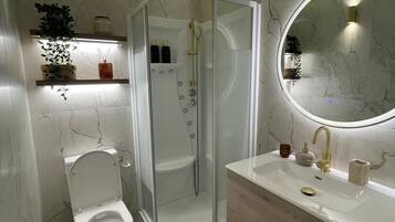 Un baño moderno con ducha envuelta en vidrio, inodoro, tocador con espejo y paredes de mármol.