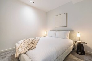 A neatly made bed with a blanket, two bedside lamps, and a framed picture on the wall. - Mordyn at Victoria Brewery Parkside Escape w Pool (East Melbourne)
