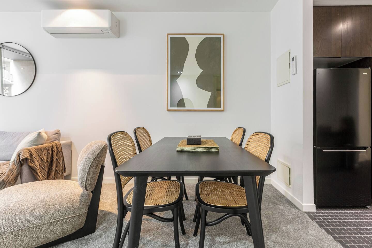 A modern dining area with a dark wooden table, wicker chairs, and a contemporary abstract painting on the wall.