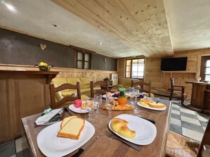 Ein Holztisch ist mit Tellern, Brot und Obst gedeckt, in einem Zimmer mit Holzwänden und einem Fernseher.