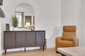 A modern living room with a dark grey cabinet, a large mirror, a potted plant, and a tan leather armchair. - Luxury Vegas Escape 4BR, Pool/Spa, Game Room & BBQ (Las Vegas)