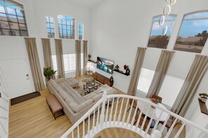 A spacious living room with a large sectional sofa, a flat-screen TV mounted on the wall, and a staircase leading to an upper level. - Luxury Vegas Escape 4BR, Pool/Spa, Game Room & BBQ (Las Vegas)