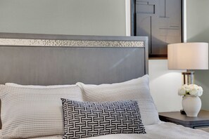 A neatly made bed with patterned pillows, a decorative headboard, a bedside table with a lamp, and a vase of flowers. - Luxury Vegas Escape 4BR, Pool/Spa, Game Room & BBQ (Las Vegas)