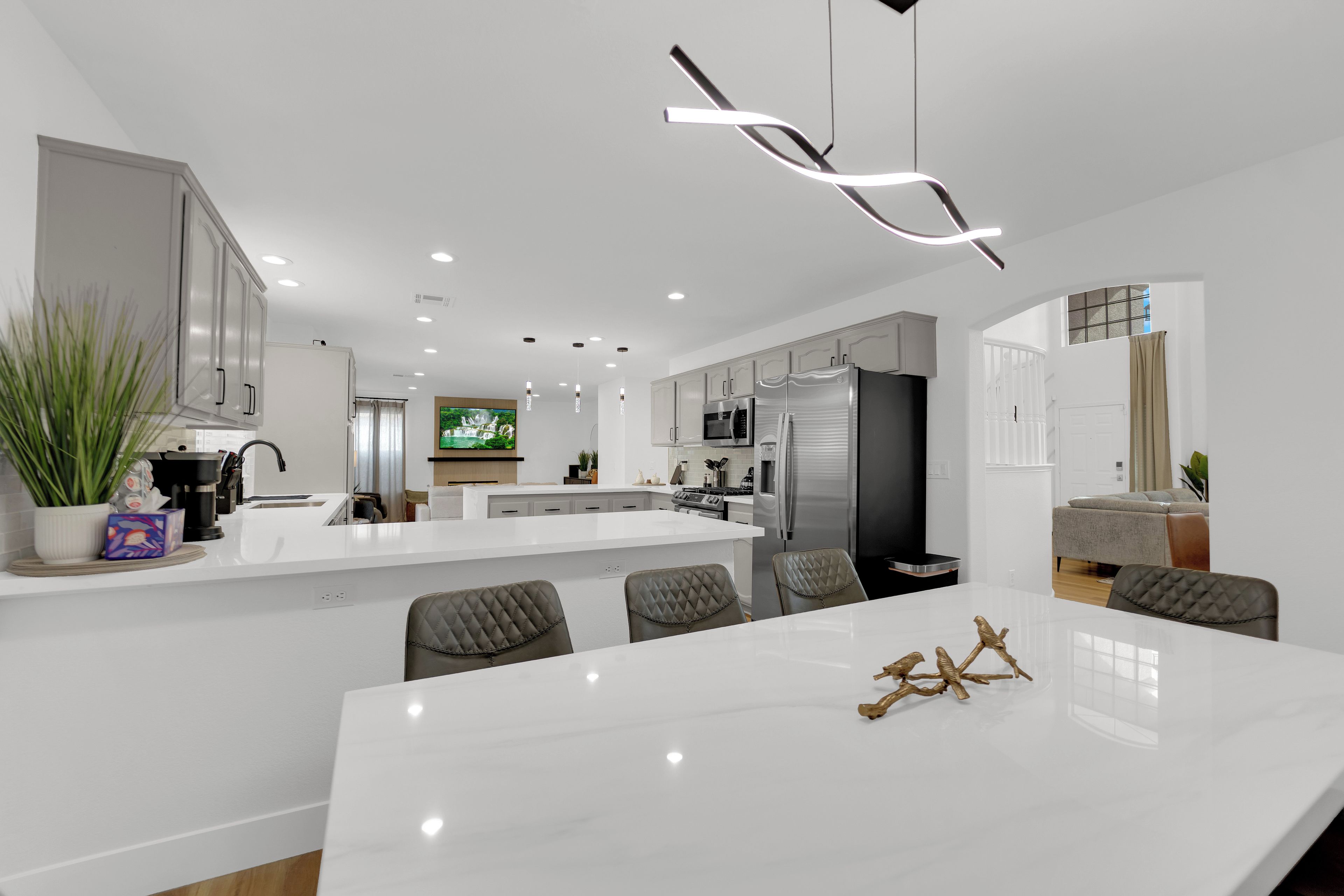A modern kitchen with white cabinetry, a central island, and a dining area with a white table and chairs.