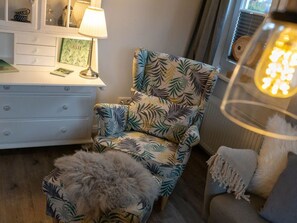 A room with a patterned armchair, a white dresser with drawers, a lamp, and a fluffy ottoman. - 1 "nordstern" in the House Gartenweg (St. Peter-Ording)