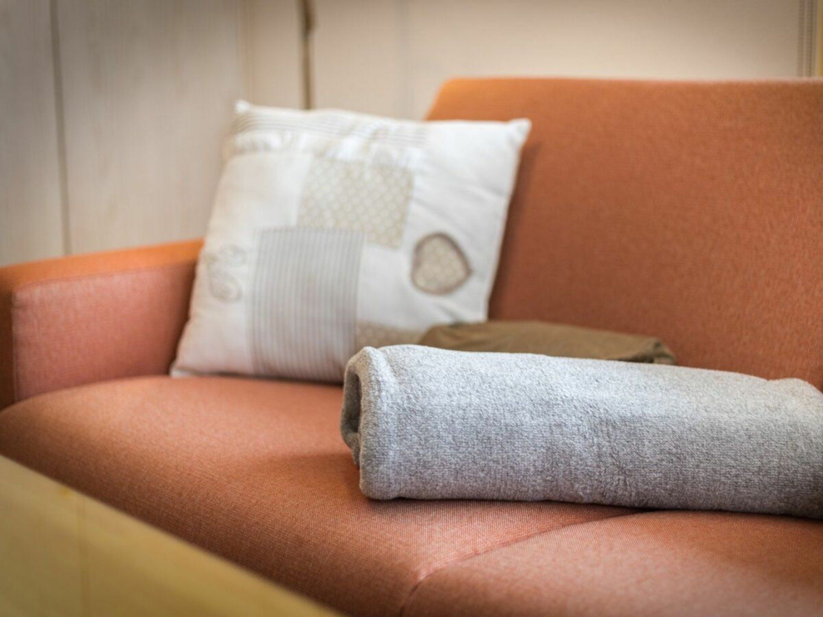 A sofa with a rolled-up grey towel and a decorative pillow.