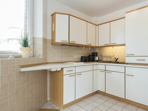 A modern kitchen with white cabinetry, a built-in oven, and a window with a plant. - 4 in the House at Blanker-hans-weg 5 (St. Peter-Ording)