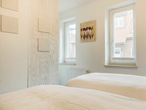 A bedroom with two beds, a radiator, and a window with a view of buildings. - 4 in the House at Blanker-hans-weg 5 (St. Peter-Ording)