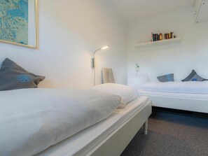 A hotel room with two beds, a bedside table, a lamp, a wall-mounted shelf with books, and a framed map. - Holiday Apartment 19 (St. Peter-Ording)