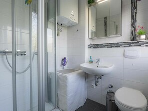 A bathroom with a glass shower enclosure, a white sink, a mirror, and a toilet. - Holiday Apartment 19 (St. Peter-Ording)