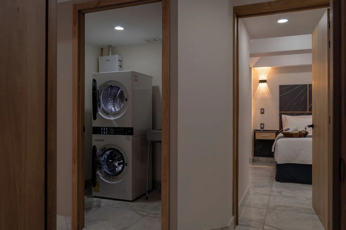 Een hotelkamer met een bed, een nachtkastje, een lamp en een wasmachine in de aangrenzende kamer.