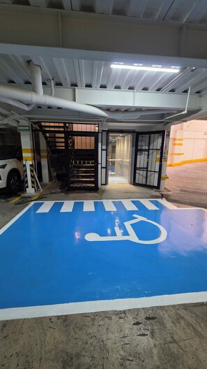 A parking garage entrance with a blue handicapped parking space, a white car, and a closed gate. - Departamento Orquídeas Elegancia, amplitud y privacidad una estancia excepcional (Ciudad de México)