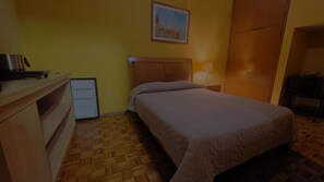 Un dormitorio con cama, mesita de noche, lámpara, armario y un refrigerador pequeño.