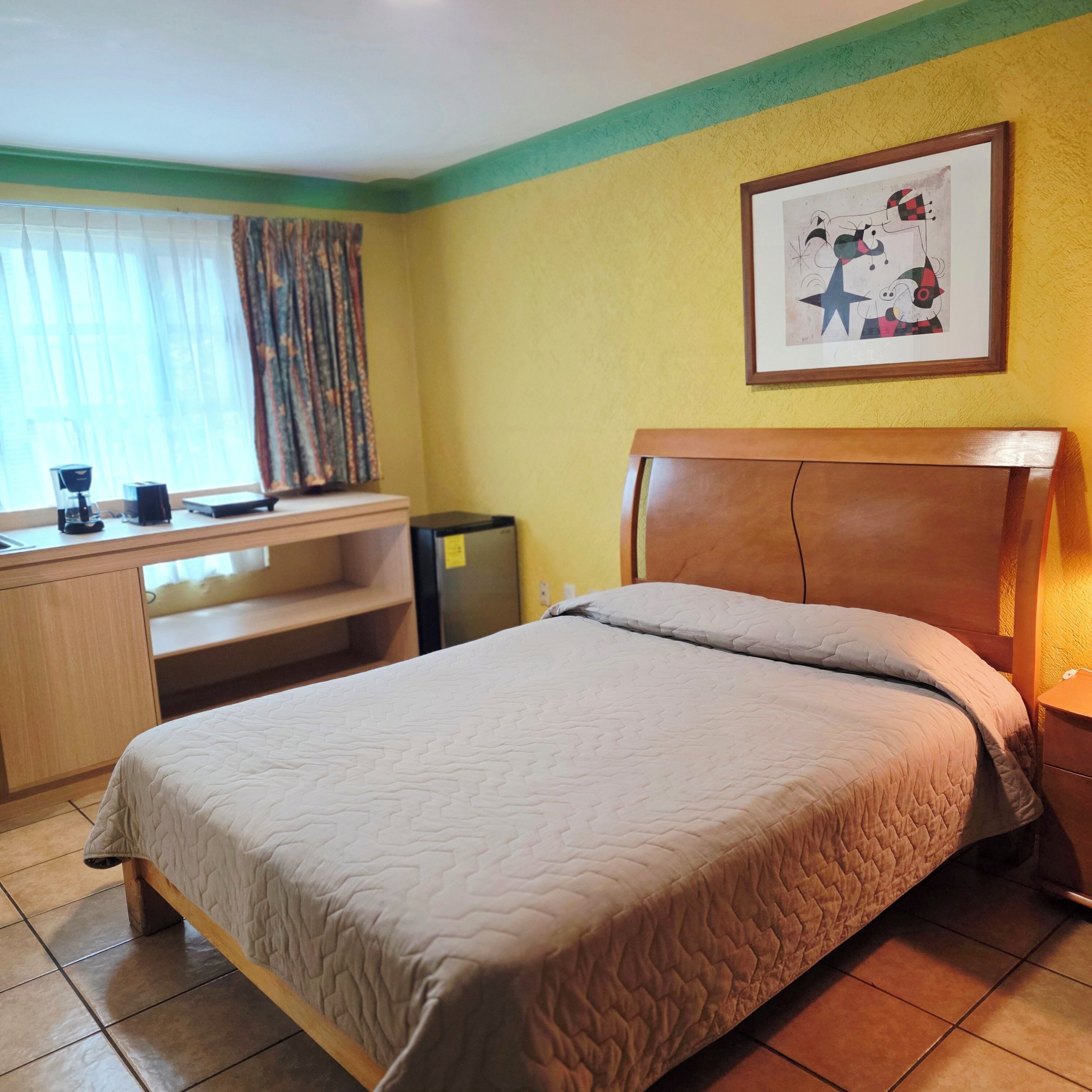 Une chambre d’hôtel équipée d’un lit, d’un bureau, d’une chaise, d’une machine à café et d’un tableau encadré au mur.