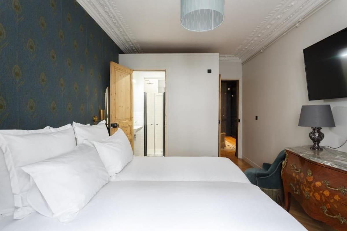 A hotel room with a large bed, a television, a desk with a lamp, and a door leading to a bathroom.