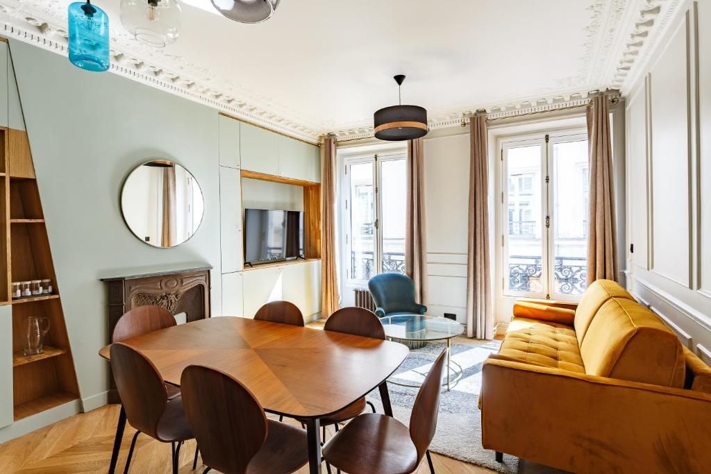 Una sala de estar moderna con una mesa de comedor, sillas, un sofá, un televisor y un ventanal con cortinas.