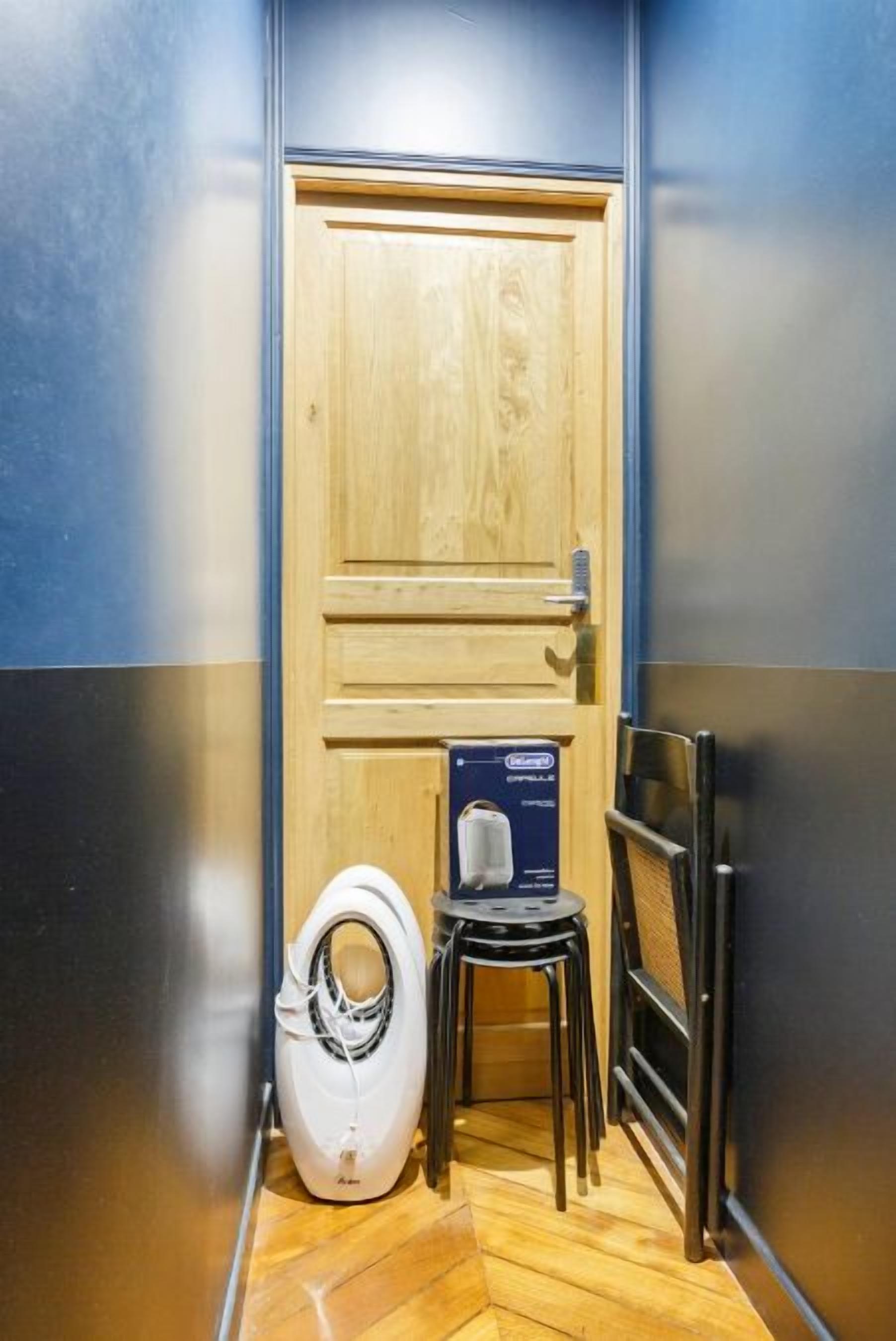 Un baño con puerta de madera, inodoro blanco y un taburete pequeño.