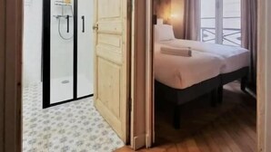 Ein Schlafzimmer mit einem Bett, einem Nachttisch, einem Fenster mit Vorhängen und einer Tür zu einem Badezimmer mit Dusche.