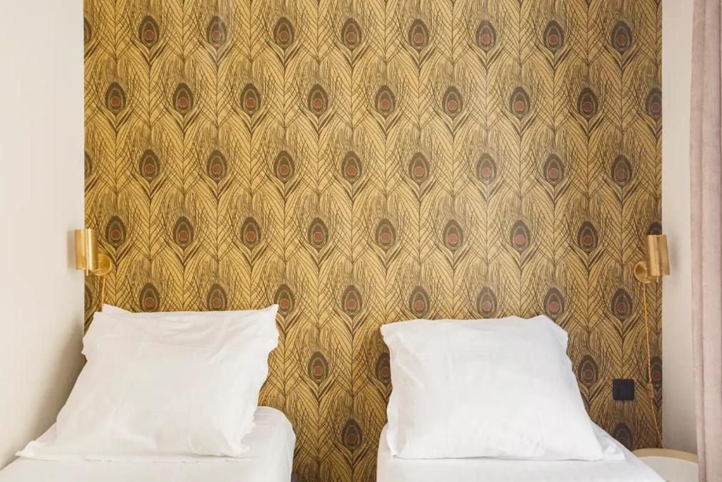 Una habitación con dos camas, cada una con ropa de cama blanca, frente a un papel tapiz estampado.