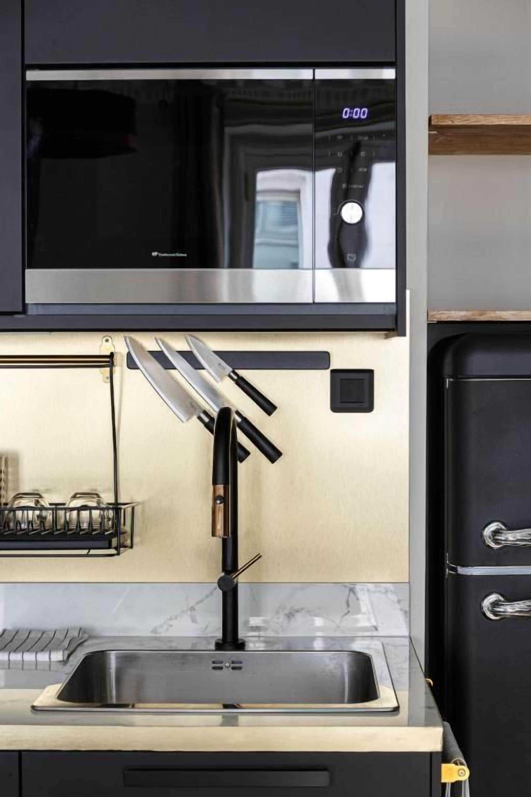 Una cocina con microondas de acero inoxidable, grifo negro y refrigerador negro.