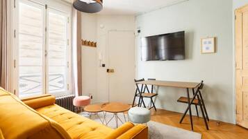 Una sala de estar moderna con un sofá amarillo, una mesa de comedor con sillas, un televisor montado en la pared y un ventanal con vistas.