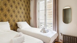 Ein Hotelzimmer mit zwei Betten, einem Fenster mit Vorhängen, einem Heizkörper und einem Spiegel an der Wand.