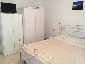 Un dormitorio con cama, armario, televisor y mesita de noche.