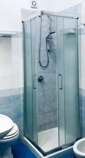 Cabina de ducha con paredes de vidrio, cabezal de ducha de mano y grifo empotrado.