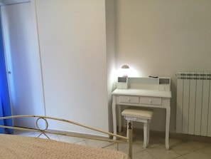 Un dormitorio con cama, un escritorio blanco con cajones, un pequeño banco y un radiador.