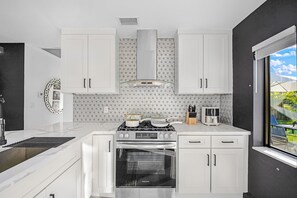 Eine moderne Küche mit weißen Schränken, einem Gasherd, einem Backofen und einer Spritzschutzwand mit geometrischen Mustern.