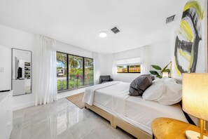 Ein modernes Schlafzimmer mit Bett, Schreibtisch und einem großen Fenster mit Jalousien.