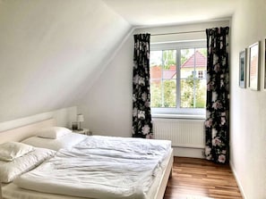A bedroom with a bed, a nightstand, a window with curtains, and a radiator. - Holiday Home in Putbus With Swimming Pool (Putbus)
