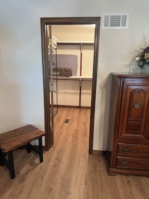 Ein Zimmer mit einer hölzernen Bank, einem Schrank und einer Tür zu einem Kleiderschrank mit einem Koffer.