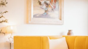Ein gelbes Sofa mit einem weißen Kissen in einem Raum, an dessen Wand ein Gemälde hängt.